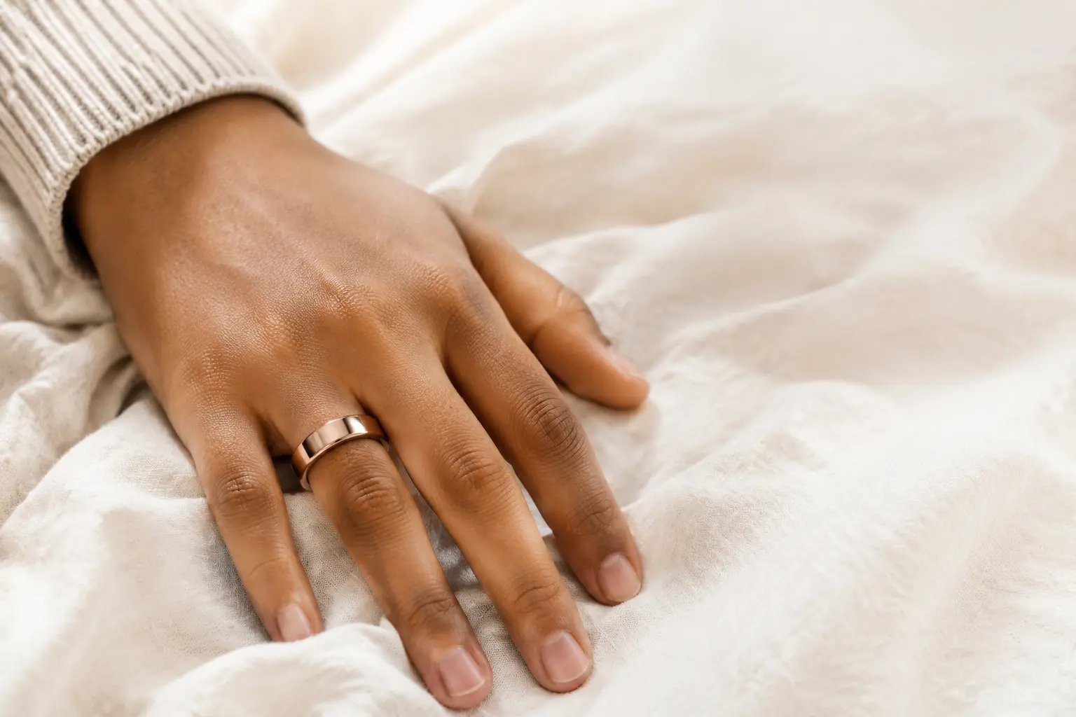Rose-gold smart ring worn while resting on soft linen